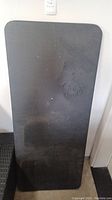 Full view of black folding table showing rectangular top with surface damage.