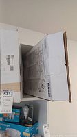 Two cardboard boxes standing upright with Kohler branding, labeled as containing two toilet seats, there is a visible inventory tag showing quantity.