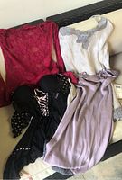 Wide view of all four lingerie items laid out on chair: red lace top, white camisole with lace trim, black polka dot bustier with pink lace-up, lavender slip with lace trim.
