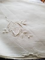 Close-up of fine dimensional floral and leaf embroidery on large white linen tablecloth