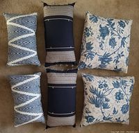 Six blue and white pillows including two rectangular navy and beige striped pillows, two blue and white zigzag patterned rectangular pillows, and two floral patterned square pillows.
