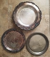 Three silver-plated trays showing varying decorative edges and cartouche designs