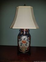 Front view of Asian style table lamp with sculpted dragon top, floral ceramic body, wood base, brass finial and silk shade