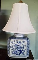 Front view of blue and white hand-painted rectangular ceramic lamp base with off-white silk shade and brass finial on top