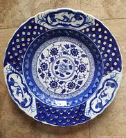 Top view of the deep blue and white decorative porcelain plate with open lattice filigree scalloped edge, floral center design, and three monkey motifs at edge panels.