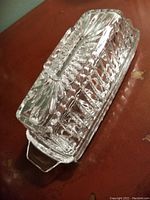 Clear cut glass butter dish with lid shown on wood surface, angled view displaying intricate cut glass design and rectangular shape with handles.