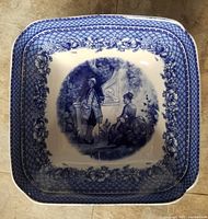 Overhead view of square deep serving bowl with central blue figurative Toile scene and floral lattice border.