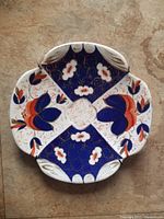 Front view of one small hand painted plate with Imari inspired red and blue floral designs and gold accents, clover scalloped edge.