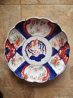 Front view of scalloped edge Imari plate showing deep set design and vivid hand painted cobalt blue and orange-red bird and floral motifs.