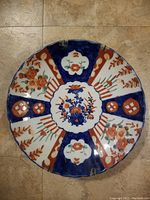 Top-down view of the full circular plate showing scalloped edges and segmented Imari floral and geometric patterns in cobalt blue, orange, and white.