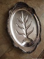 Top view of silver plated oval serving platter with embossed tree design and ornate raised edge