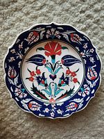 Front view of hand-painted Turkish Iznik style wall plate showing detailed floral motifs in cobalt blue, red, turquoise, and white on ceramic scalloped plate.