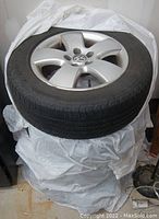 Stacked Goodyear tire on VW alloy rim against a white wall, showing tread and rim design.