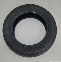 Photo showing one black rubber Winter Claw Extreme Grip tire, size 195/50 R15, placing the tire flat on the ground to show tread and sidewall details.