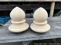 Two new wooden bed post tops placed side by side on a weathered wooden surface.