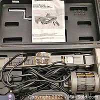 Electric scissor car jack in a plastic carrying case with power cables, crank handle, and instruction manual.