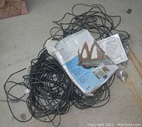 Coiled black electrical heating cable with instruction manual and packaging for roof eave de-icing system spread on floor.