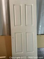 Photo of a white six-panel interior door leaning against surface showing full door front with minor scuffs and marks.