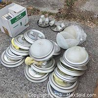 15 aluminum surface-mount ceiling light fixtures stacked on the ground with some globes separated and packed. Various fixtures include some with frosted domed glass covers and some missing globes. Fixtures have a silver aluminum finish.