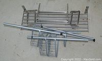 Photo showing multiple metal shelving components including frames, racks, and support brackets collected on floor.