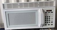 Front view of a white Danby microwave showing the door with mesh viewing window and digital control panel with buttons.