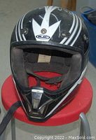 Front view of black and white HJC motocross helmet with visible interior and chin strap on red stool.