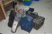 Photo of backpacks, rolling bags, rolled tent or mat, black fleece jacket, and other packed camping gear on floor