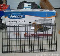 New Petmate Training Retreat dog cage with its original box and two detached wire extension panels in front. Partially visible black soft-sided pet carrier tote behind the box.