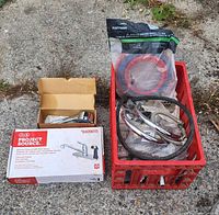 Photo showing Project Source kitchen faucet in box and a red crate containing miscellaneous plumbing fixtures including hoses, fittings, chrome handles, and packaged rubber washers.