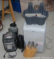 Premiere branded dehumidifier in white with cords and power strip on top, electric kettle, coffee maker, and garbage disposal unit arranged on floor