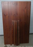 Top view of a rectangular brown stained wooden table surface with four detached table legs placed on top.