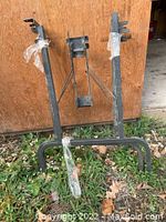 Photo of two metal folding table legs leaning against wooden wall outdoors