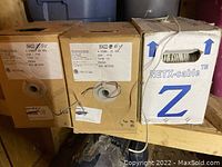 Three partial cardboard boxes of 4 conductor 22 gauge solid telephone wire, including two labeled boxes with product details and one NETX-cable box with exposed wire.