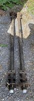 Two 72-inch trailer axles with hubs and brake backing plates laid side by side on gravel