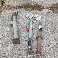 Two used trailer jacks laid on concrete with mounting plates visible.