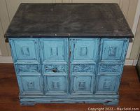 Front view of a painted wood chest showing blue distressed panels and worn dark wood top surface
