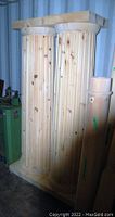 Two tall fluted wood columns side by side in a storage setting, showing natural wood grain and knots, with bases and capitals visible.