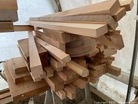 Stack of assorted wood offcuts including rectangular and square rods, flat boards, and curved wood pieces piled on a shelf.