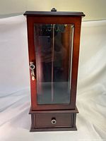 Front view of tall dark wood jewelry display case with glass door and central vertical divider inside.
