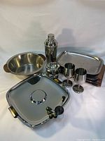Photo of chrome dish set including serving trays, bowls, wine glasses, cocktail shaker, and pitcher arranged on white background