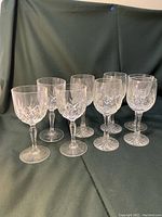 Group of 8 crystal wine glasses with cut starburst design, standing upright against black background.