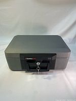 Front view of the gray hard plastic safe briefcase showing black handle with key lock and key inserted.