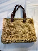 Front view of wicker basket handbag showing woven texture and brown faux leather straps