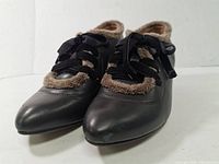 Pair of black leather women's kitten heel shoes with brown fur trim and black satin ribbon laces viewed from front.