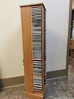 Full view of the revolving CD tower fully loaded with CDs on all sides, wood finish, standing on floor.