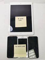 Photo of one white Apple iPad and three black iPhones, all powered on but with sticky notes indicating no access codes