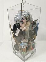 Full view of clear rectangular 8 inch glass vase filled with mixed costume jewelry including beads, chains, bracelets, and bangles in various colors and materials.