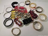 Top-down view of many bracelets and bangles in silver, gold, black, and multicolor beads piled together on white background.