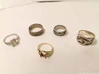Five rings displayed in a row on white background, showing varying designs and materials.