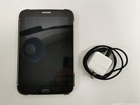 Samsung Galaxy Note 8.0 tablet with Samsung case, charging cord, and wall charging unit laid out showing front screen and accessories.